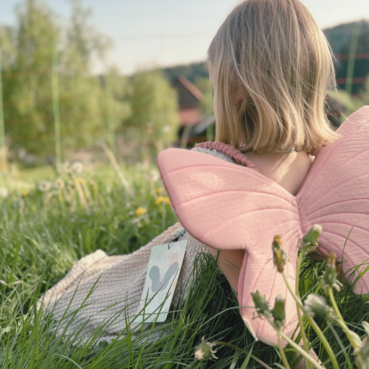 Kind trägt Schmetterlingsflügel Feenflügel bei Kindergeburtstag während Schatzsuche und sitzt im Gras